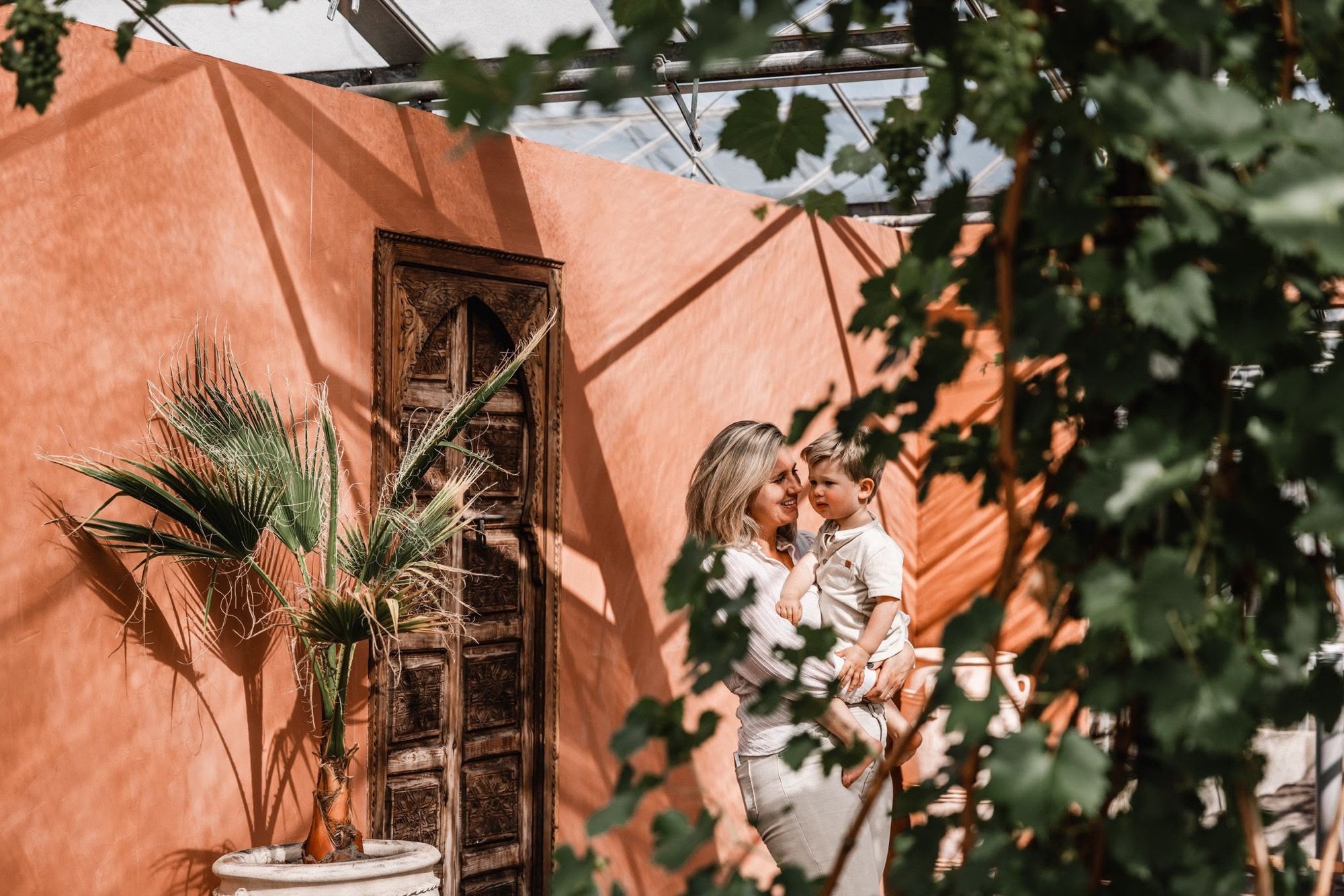 Moeder en kind tussen de bladeren, het zonlicht en de terracotta muren
